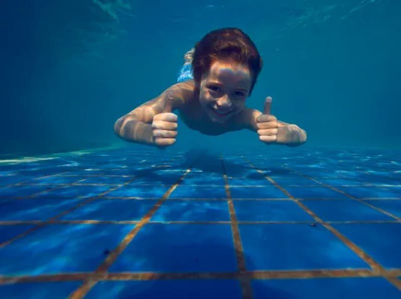Menino mergulhando e fazendo sinal de positivo debaixo d’água na piscina do Lagos de Jurema